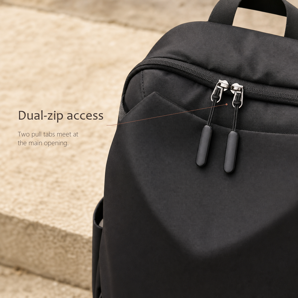 CommuteCore structured laptop backpack in black, close-up of the dual-zip access with two metal pull tabs meeting at the main opening.