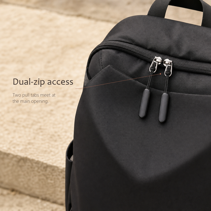 CommuteCore structured laptop backpack in black, close-up of the dual-zip access with two metal pull tabs meeting at the main opening.