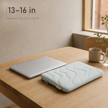 TerraSleeve laptop sleeve in cloud mist, laid beside a silver laptop on a wooden table beside a mug, showing the 13-16 in fit.