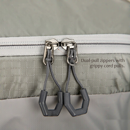 TrailFrame 75L hiking backpack in sage gray-green, extreme close-up of the top-lid zipper showing dual metal sliders with dark gray cord pull loops.